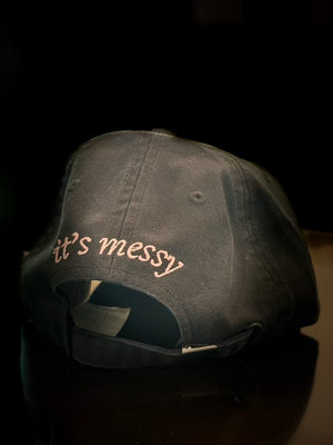 Back of the black Scatter dad hat, with “it’s messy” embroidered across the back